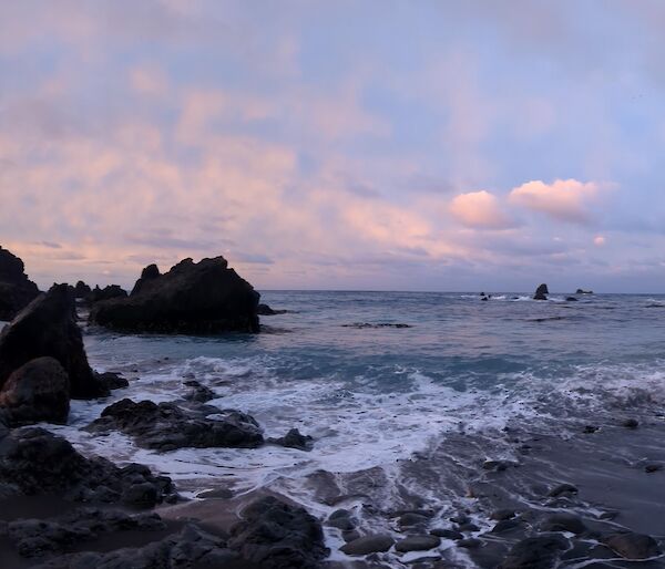 An orange glow in clouds over the ocean and coastline of Macquarie Island.