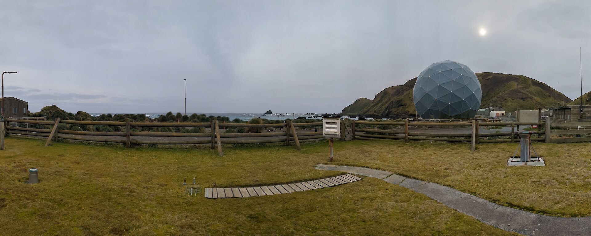 A panoramic view of huts and weather instruments installed on flat, vegetated ground at Macquarie Island.