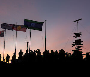 Mawson station expeditioners silhouetted against dawns light as they begin their service under the flagpoles