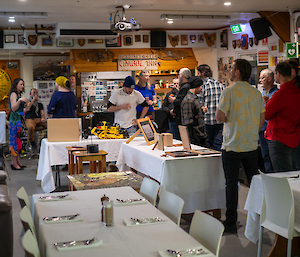 A group of people stand around in a dining room looking at art on a table.