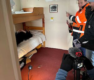 One person films while another looks at the camera in a bunkroom.