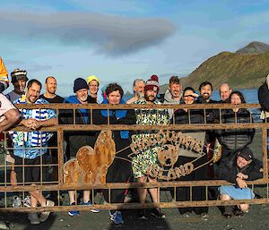 People stand behind a gate with hills and blue sky behidn them.