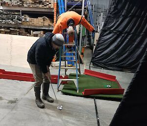 People play minigolf in a warehouse.