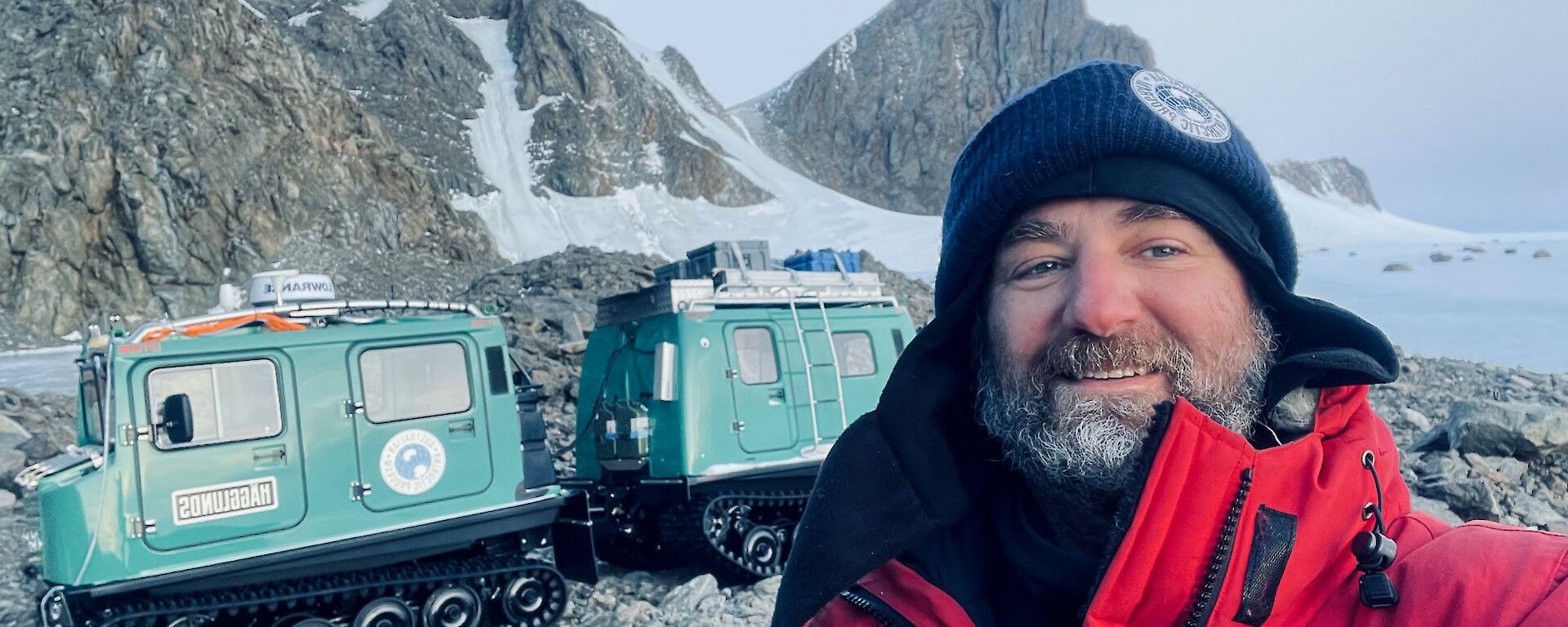 A selfie of Richard Heaton out in the Framnes Mountains near Mawson station with a green Hagglunds in the background