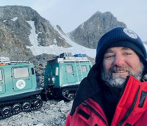 A selfie of Richard Heaton out in the Framnes Mountains near Mawson station with a green Hagglunds in the background
