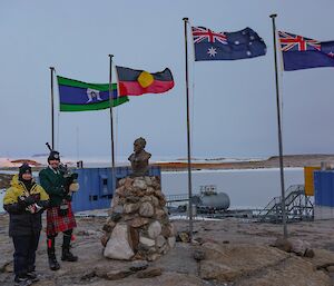 Bagpipe player Peter Caithness and trumpet player Sophie Counsell under the four flags flying at Mawson for ANZAC Day