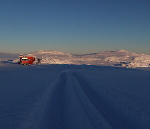 A red hut in the distance with snow and rock escarpment in background on horizon