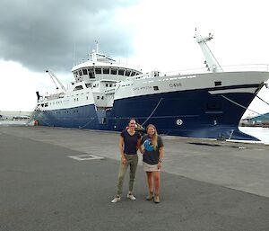 Two women standing beside a blue and white fishing vessel.