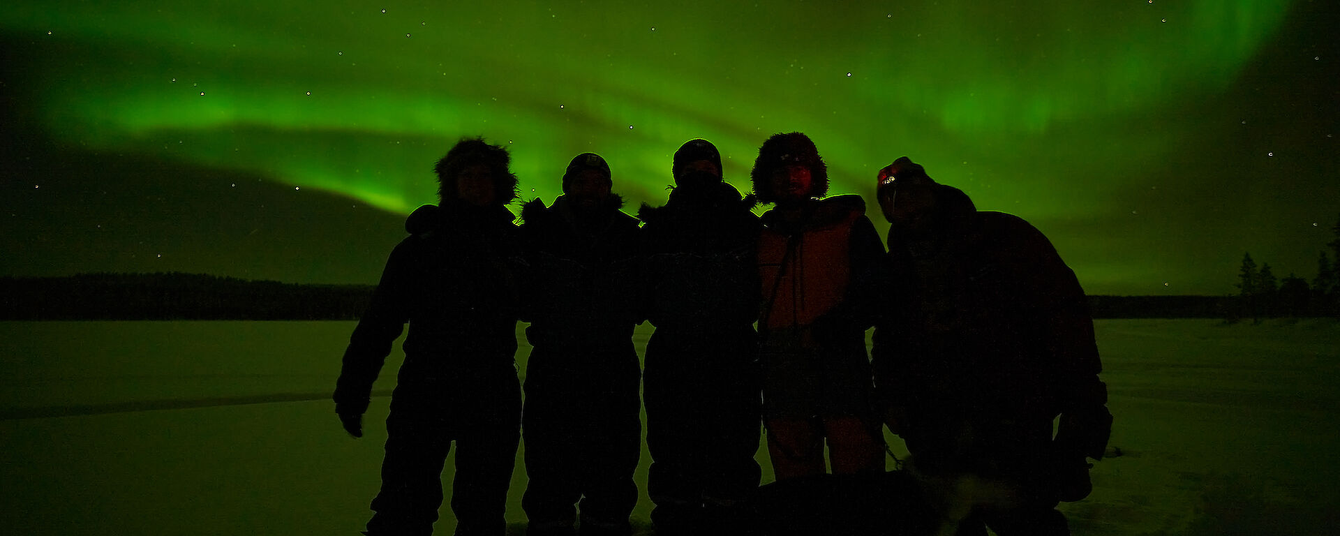 5 people silhouette foreground to a vibrant Aurora Borealis
