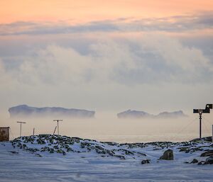 a view of Wilkes station old infrastructure in the foreground with large icebergs to the background encapsulated in sea smoke.