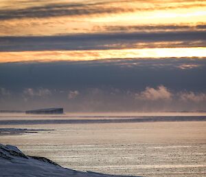 Sea smoke and associated fractostratus cloud west of the Bailey Peninsula, icebergs in background with colors associated with the setting of the sun piercing through clouds