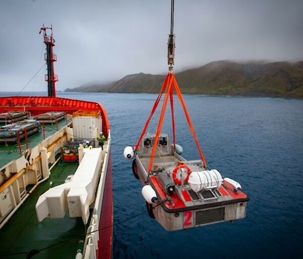 A LARC is lowered over the side of a ship with a crane.