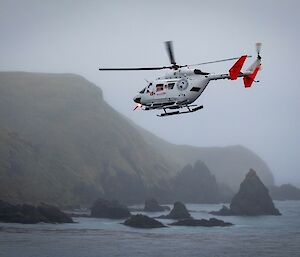 A helicopter flies towards the rocky coast of Macquarie Island