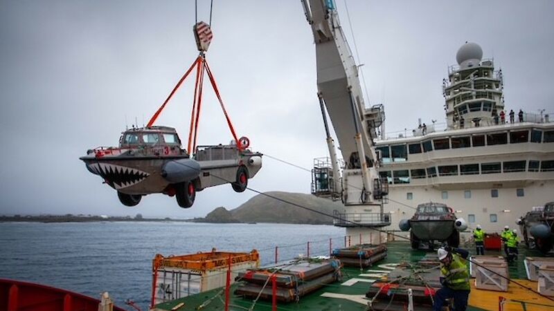 A metal boat with teeth painted on the front is lowered from a ship by crane