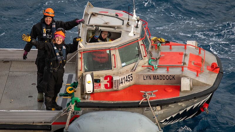 two people in dry suits stand on a boat