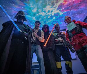 A view from the ground looking up at 5 members with terrific star wars costumes, galactic style lights in background