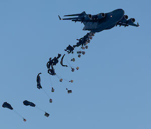 Thirty-one bundles of supplies and equipment fall from the aircraft with parachutes beginning to open