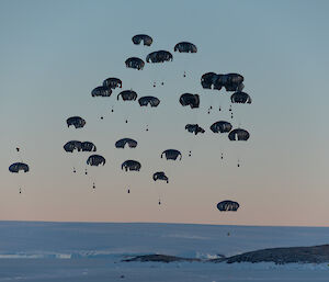 A winter view with the sky full of black parachutes with cargo loads beneath