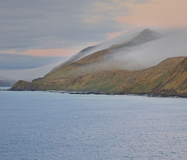 Mist-covered peaks on the hillside of an island, sea in the foreground