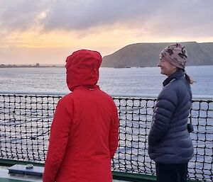 A woman in a red parka standing on a ship's deck with a woman in a black puffer.