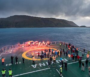 Flares are set off by people standing on a ship's helicopter deck.
