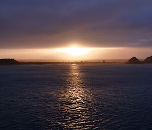 Sunset under cloud with sea in the foreground.