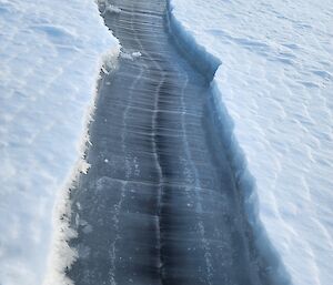 A cleared line of dark blue ice beneath white snow