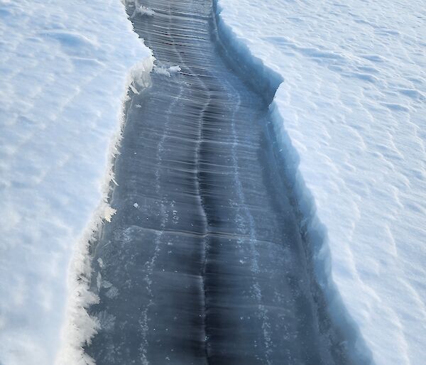 A cleared line of dark blue ice beneath white snow
