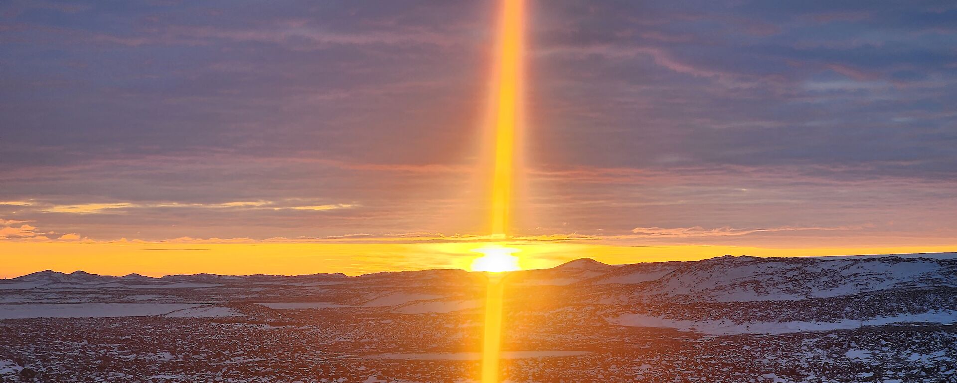A sunset over snow-covered rocks. The sunlight appears as a vertical bend of orange light dividing the photo in half.
