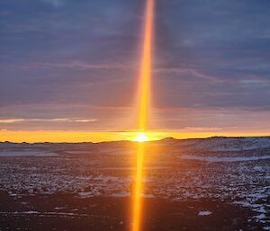 A sunset over snow-covered rocks. The sunlight appears as a vertical bend of orange light dividing the photo in half.