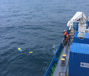 Crew members on the deck of a ship haul an oceanographic instrument used to record underwater sound through the water to bring it aboard.