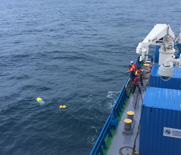 Crew members on the deck of a ship haul an oceanographic instrument used to record underwater sound through the water to bring it aboard.