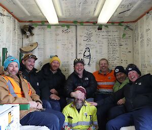 Eight people sitting closely together inside a shipping containing with lots of writing on its walls.