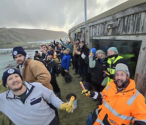 Group of expeditioners on deck of hut overlooking isthmus, smiling and looking to camera