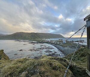 Looking from height beside wooden hut across the island isthmus of black sand, and distant buildings with a large mountain at the other end of the isthmus in the distance