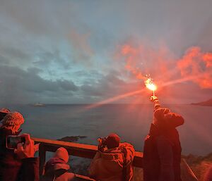 Taken from behind, an expeditioner holds aloft a lit flare