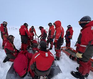 the full team gathered around the stretcher wearing vibrant red mustang suits down by the wharf