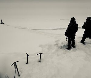 a black and white image on three expedtioners feeding out rope as the rescue alive pontoon is taken out onto the sea ice