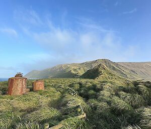Tussock covered ground to mountain in the background. Rusted old seal digesters in the left foreground.