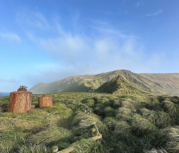 Tussock covered ground to mountain in the background. Rusted old seal digesters in the left foreground.