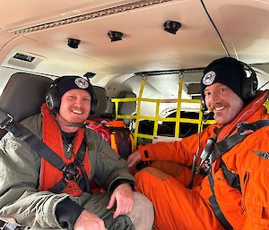 Rear of helicopter cab with two men sitting smiling to camera