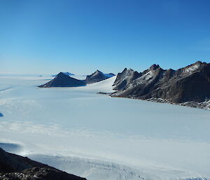 A snowy flat plain with grey jagged mountains in the background