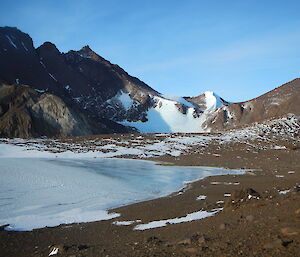 An icy lake in the foreground brown hills around covered in snow