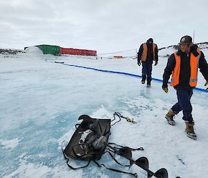two expeditoners on lake ice drilling holes for a water transfer