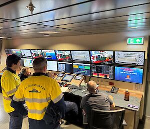 Five people watch a panel of monitors  showing various images and scientific statistics during an instrument deployment.