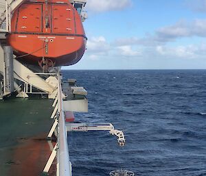 A cylindrical instrument containing a rosette of bottles is lowered by a small crane from the side of a ship.