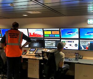 Three people look at a bank of monitors showing video and scientific statistics of a net being deployed behind a ship.