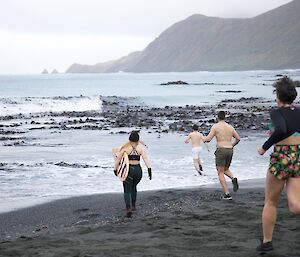 Group of expeditioners running down the beach into the water, one holding the surf board