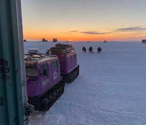 three expeditioners kick their feet up on the ice viewing the setting of the sun on deck chairs