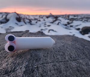 A white device sits on a rock with snow in the background
